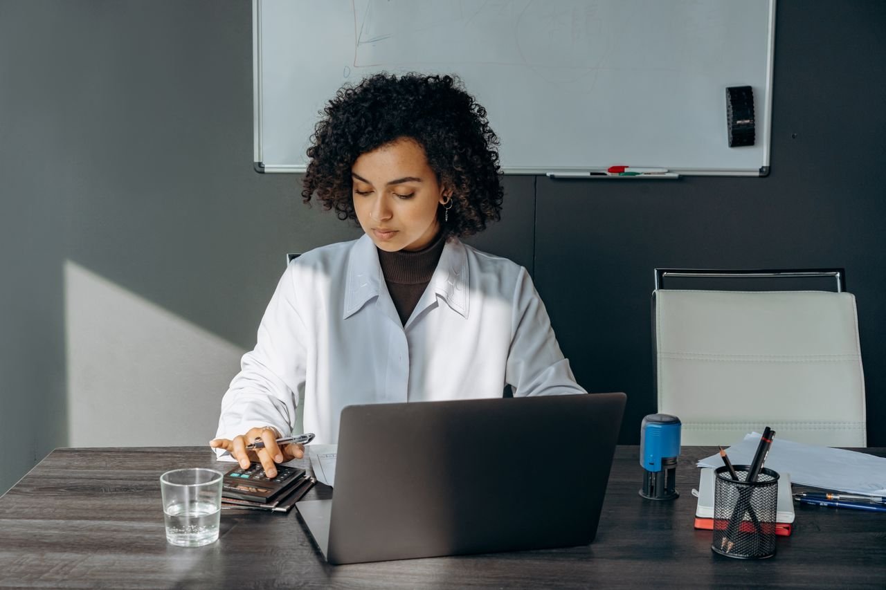 Mastering the First Impression: Your intriguing post title goes here Focused woman in office setting working on laptop with documents, creating a professional atmosphere.